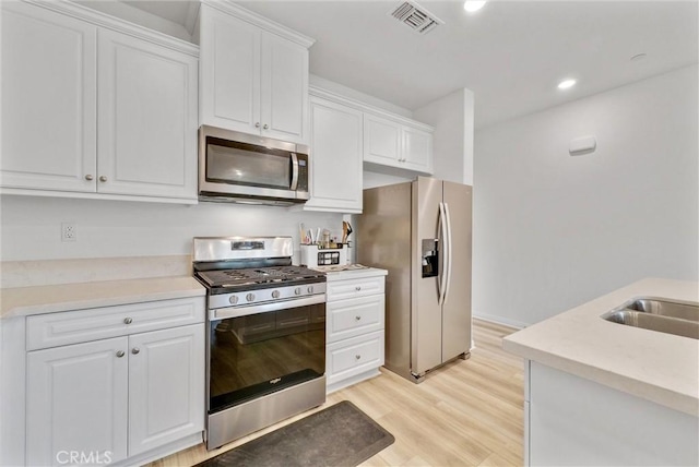 kitchen featuring stainless steel appliances, white cabinets, and light wood-type flooring