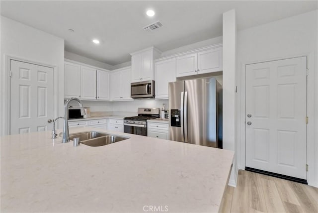 kitchen with light stone countertops, light hardwood / wood-style floors, white cabinetry, appliances with stainless steel finishes, and sink