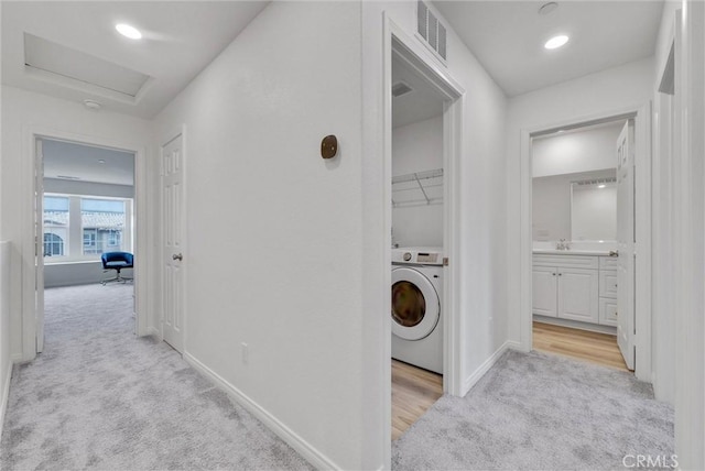 hallway with washer / dryer, sink, and light carpet