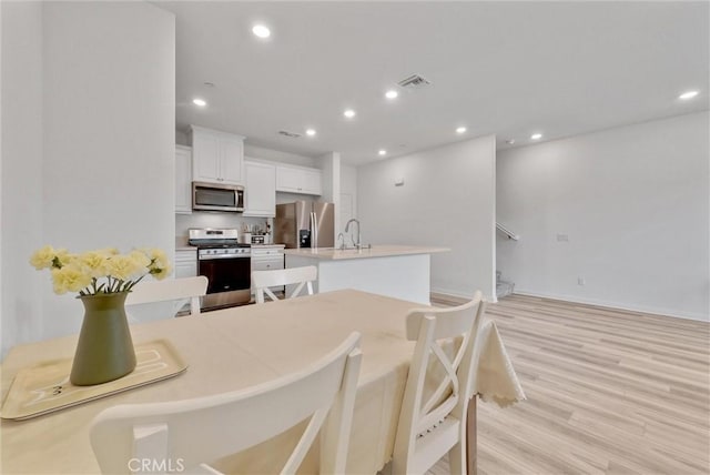 kitchen with appliances with stainless steel finishes, light wood-type flooring, an island with sink, sink, and white cabinetry