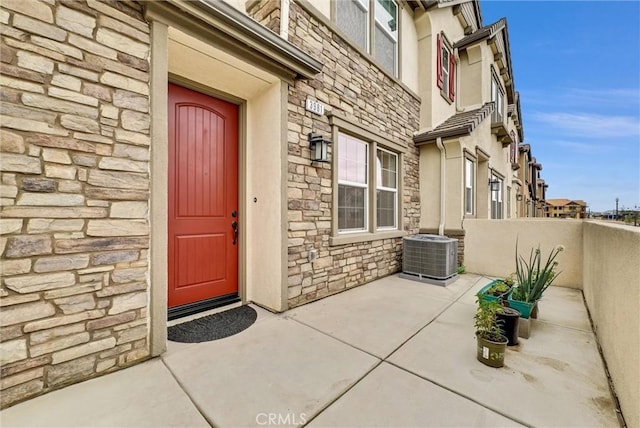 view of exterior entry featuring central air condition unit and a patio area