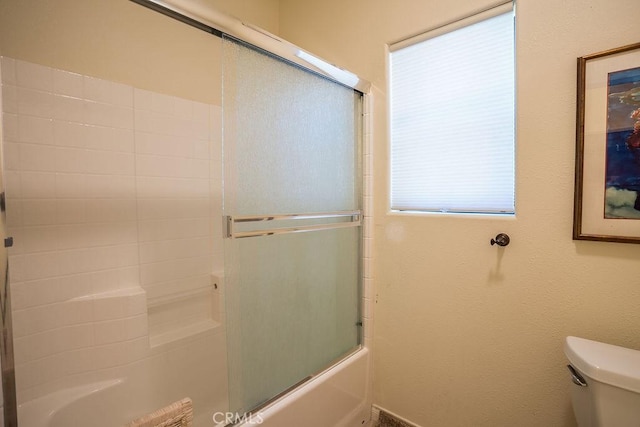 bathroom with toilet and shower / bath combination with glass door