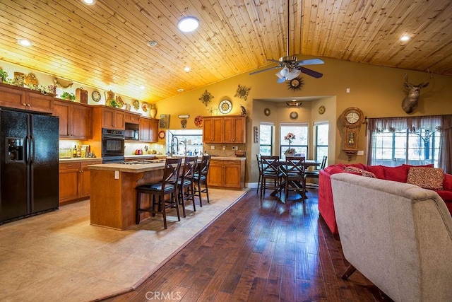 kitchen with a center island, wooden ceiling, a kitchen bar, black appliances, and hardwood / wood-style flooring