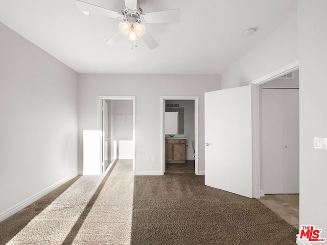 unfurnished bedroom with dark colored carpet, ensuite bathroom, ceiling fan, and a walk in closet