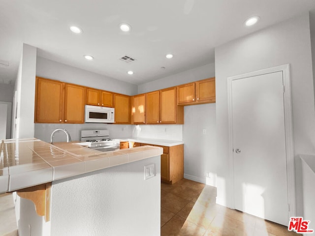 kitchen featuring tile countertops, a center island, light tile patterned floors, and white appliances