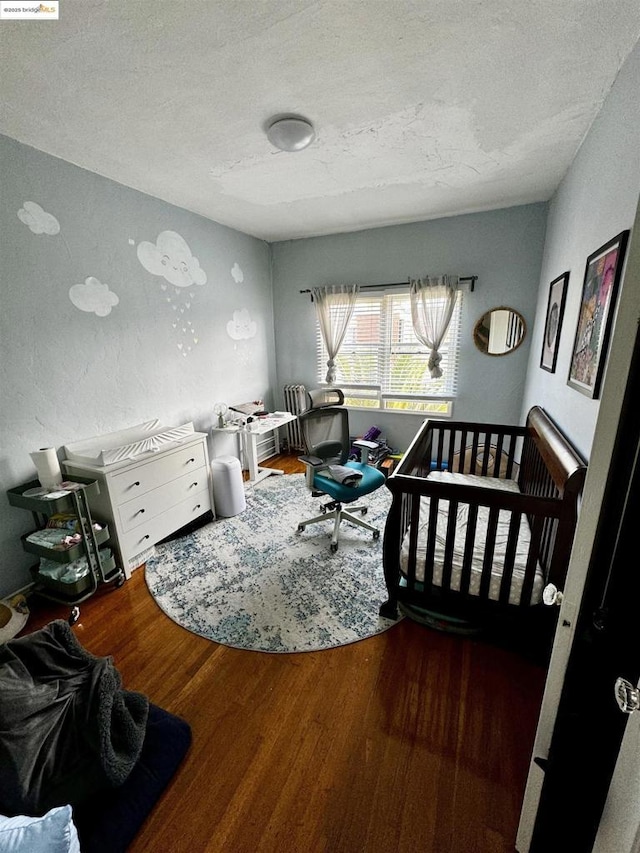 bedroom featuring wood-type flooring, a textured ceiling, and a nursery area