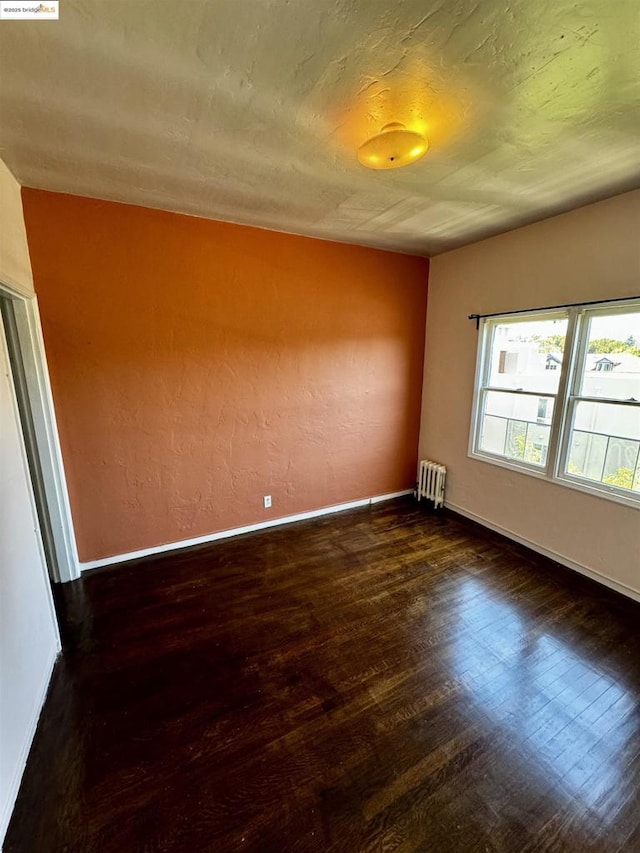 empty room with radiator heating unit and dark hardwood / wood-style floors