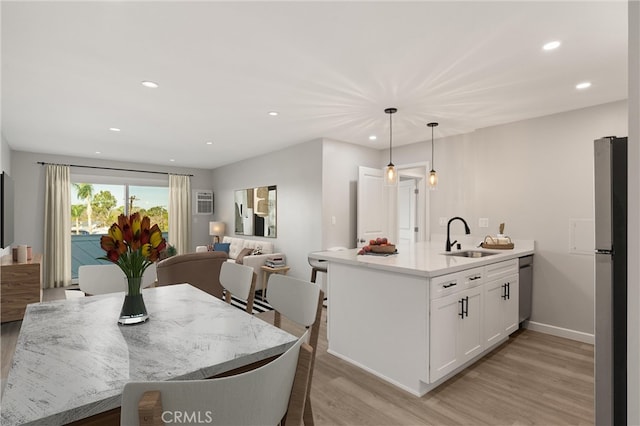 kitchen with a peninsula, a sink, white cabinetry, appliances with stainless steel finishes, and light wood-type flooring