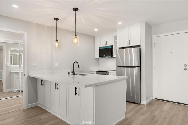 kitchen with light wood finished floors, freestanding refrigerator, a peninsula, black microwave, and a sink