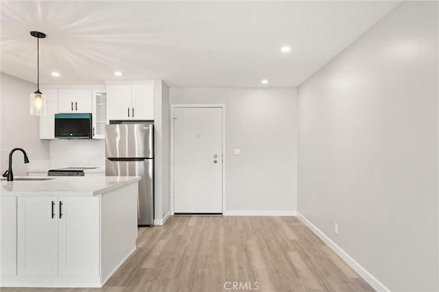 kitchen with light countertops, light wood-style flooring, freestanding refrigerator, white cabinetry, and a sink