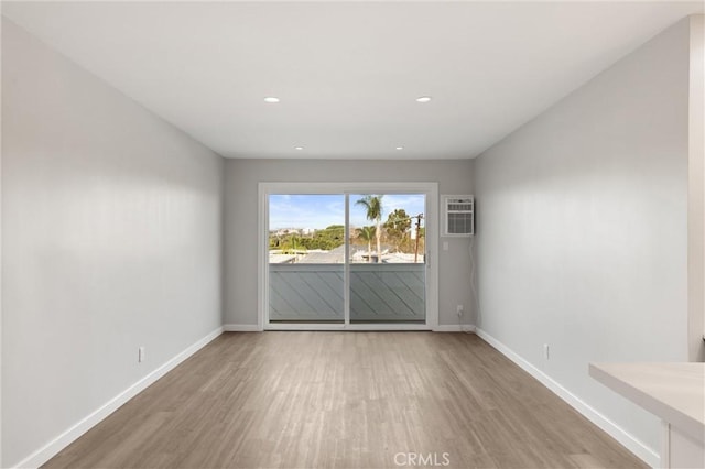 spare room featuring light wood-style floors, recessed lighting, a wall unit AC, and baseboards