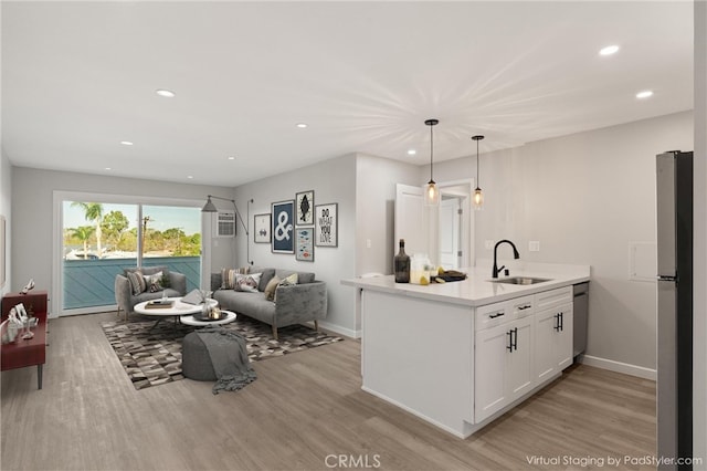 kitchen with sink, appliances with stainless steel finishes, white cabinetry, decorative light fixtures, and light wood-type flooring