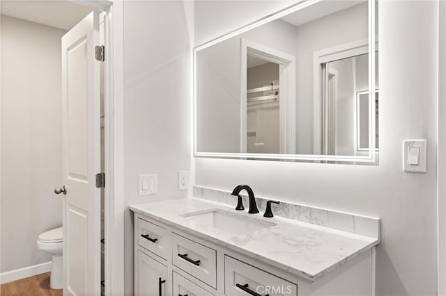 bathroom featuring toilet, baseboards, wood finished floors, and vanity