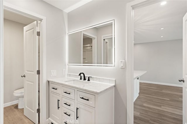 bathroom with recessed lighting, toilet, vanity, wood finished floors, and baseboards