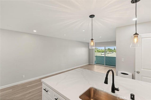 kitchen with light wood finished floors, baseboards, white cabinets, hanging light fixtures, and a sink