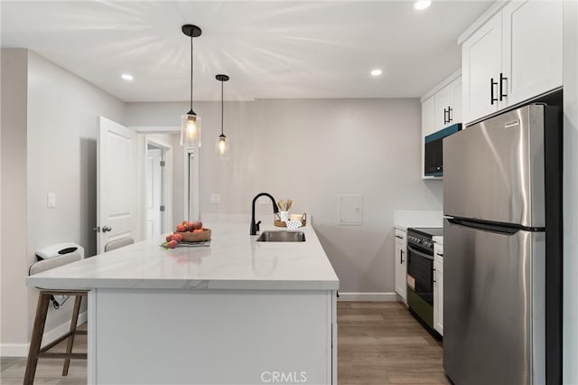 kitchen with light wood-style flooring, stainless steel appliances, a kitchen bar, white cabinetry, and a sink