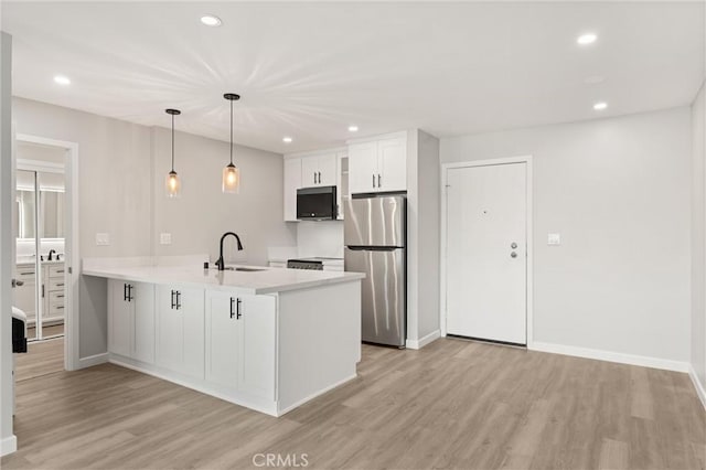 kitchen featuring a peninsula, light wood-style flooring, a sink, and freestanding refrigerator