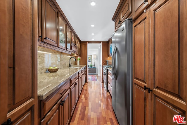 kitchen featuring backsplash, sink, light wood-type flooring, appliances with stainless steel finishes, and light stone counters