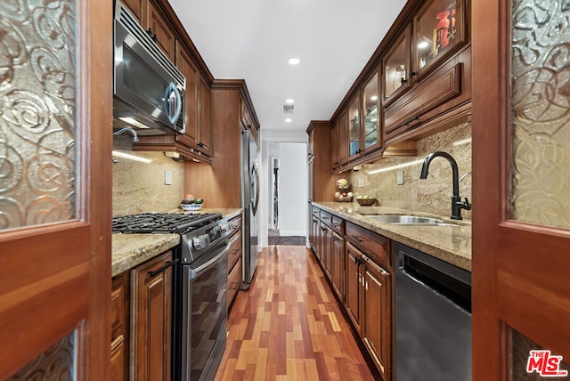 kitchen with light stone countertops, sink, tasteful backsplash, light hardwood / wood-style flooring, and appliances with stainless steel finishes