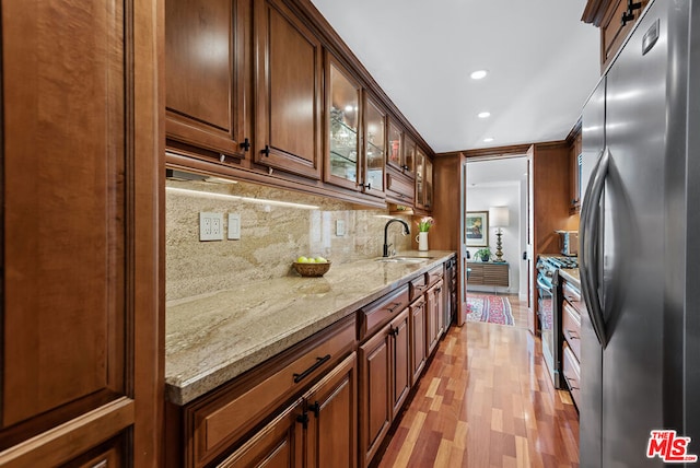 kitchen with light stone countertops, sink, stainless steel appliances, tasteful backsplash, and light hardwood / wood-style floors