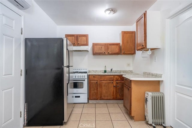 kitchen featuring radiator, gas stove, stainless steel fridge, light tile patterned floors, and a wall mounted air conditioner