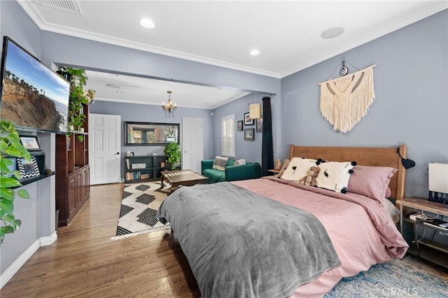 bedroom with hardwood / wood-style flooring, ornamental molding, and an inviting chandelier