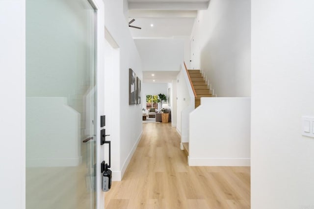 corridor with beam ceiling, light hardwood / wood-style floors, and a high ceiling