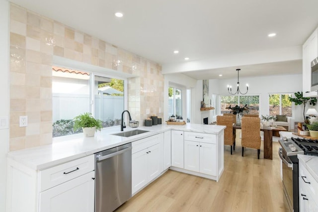 kitchen with white cabinets, sink, light hardwood / wood-style floors, stainless steel appliances, and a chandelier