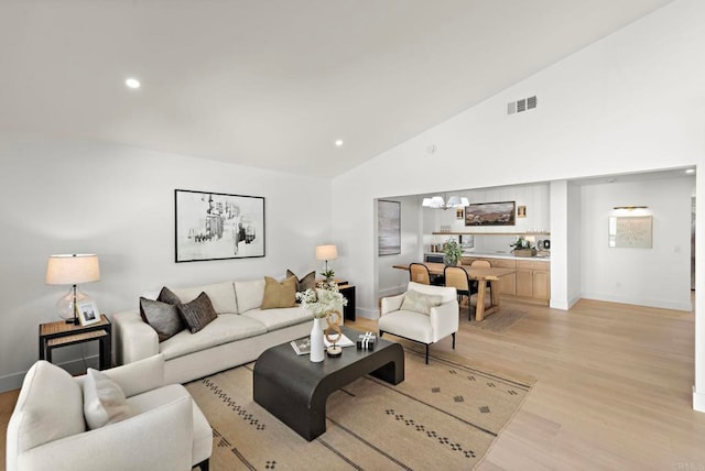 living room with high vaulted ceiling, light wood-type flooring, and an inviting chandelier