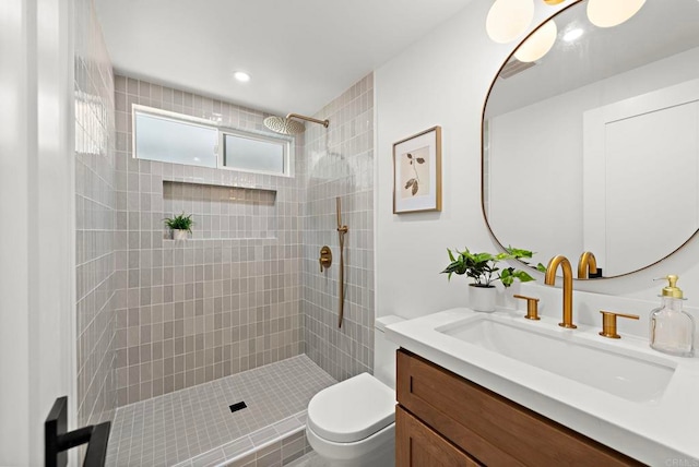 bathroom with a tile shower, vanity, and toilet