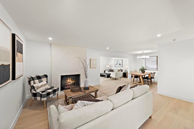 living room with a large fireplace, light hardwood / wood-style flooring, and a notable chandelier