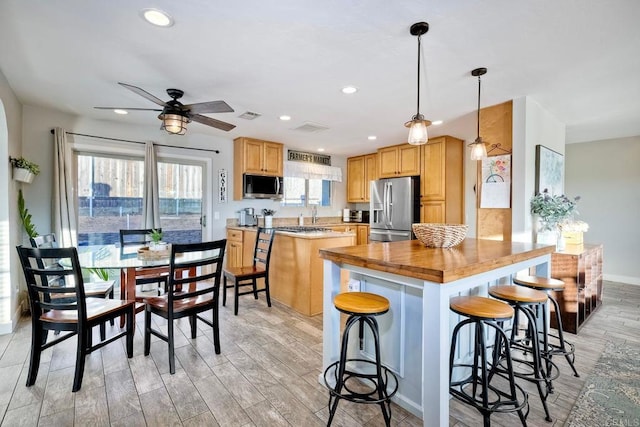 kitchen with ceiling fan, stainless steel appliances, wooden counters, decorative light fixtures, and a kitchen bar