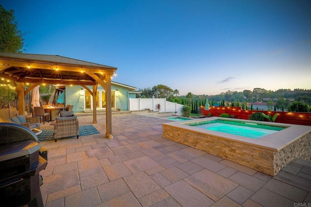 pool at dusk featuring a gazebo, an in ground hot tub, and a patio