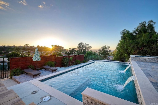 pool at dusk with pool water feature and a patio