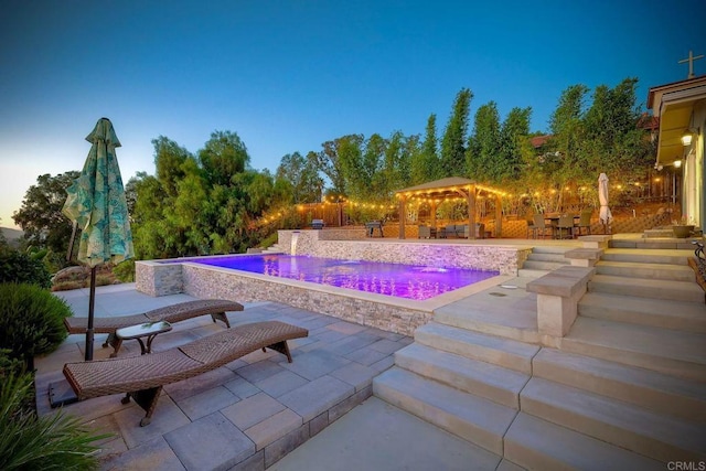 pool at dusk with a pergola, pool water feature, and a patio area