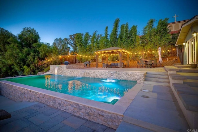 pool at dusk with a gazebo, pool water feature, a bar, and a patio