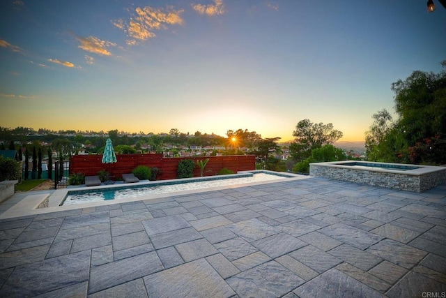 pool at dusk with an in ground hot tub and a patio