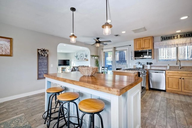 kitchen with wooden counters, appliances with stainless steel finishes, sink, decorative light fixtures, and a kitchen island