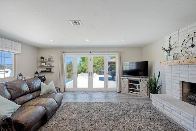 living room with french doors, light hardwood / wood-style floors, and a brick fireplace