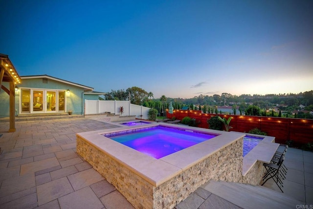 pool at dusk with an in ground hot tub, a patio, and french doors