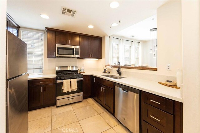 kitchen featuring dark brown cabinets, stainless steel appliances, sink, light tile patterned floors, and decorative light fixtures