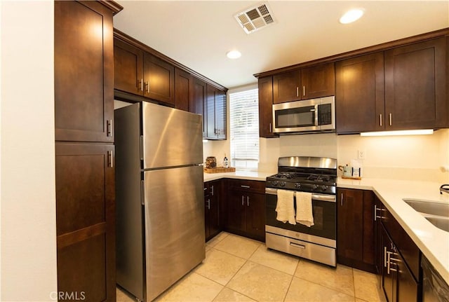 kitchen with dark brown cabinetry, sink, stainless steel appliances, and light tile patterned flooring