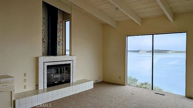 unfurnished living room featuring beam ceiling, a tile fireplace, wooden ceiling, light colored carpet, and a water view