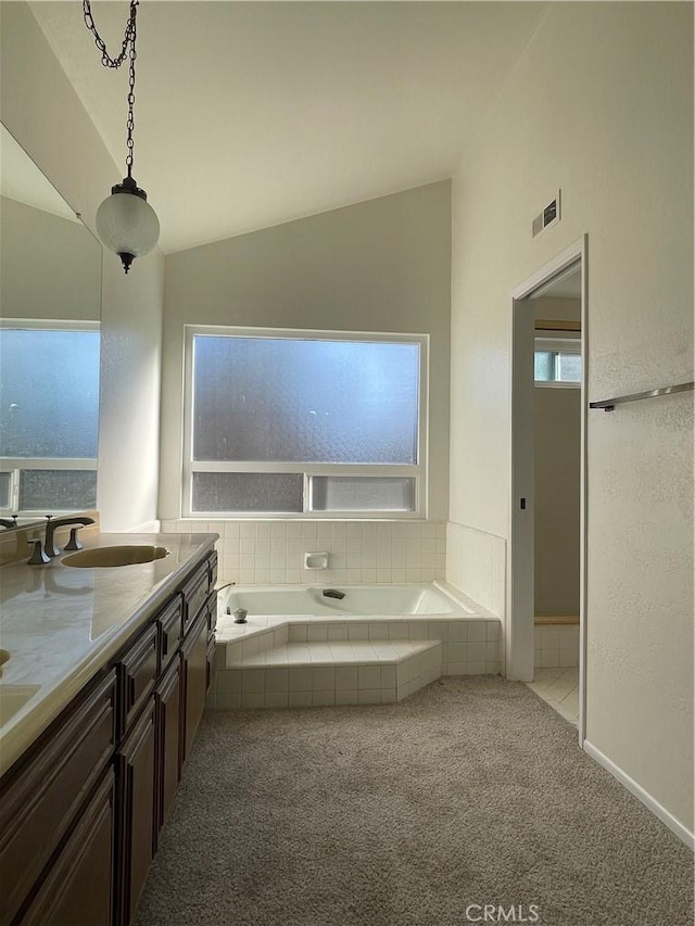 bathroom featuring vanity, tiled tub, and vaulted ceiling