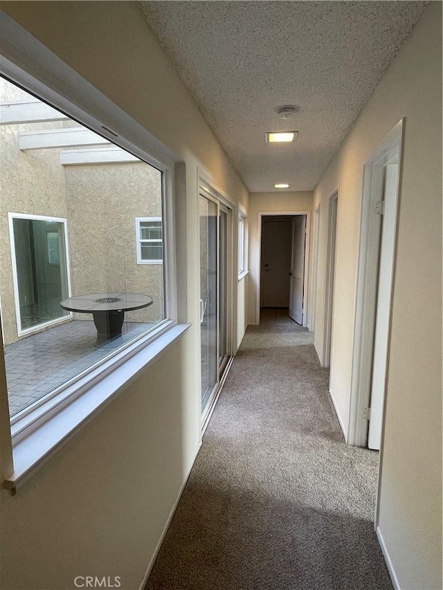 hallway featuring light colored carpet and a textured ceiling