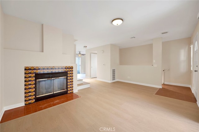 unfurnished living room with a tile fireplace, hardwood / wood-style flooring, and ceiling fan