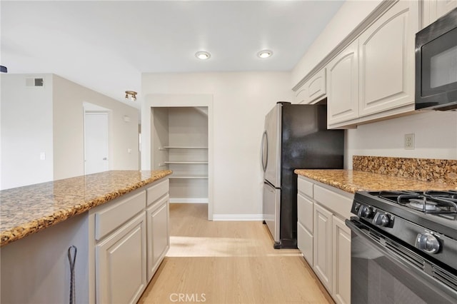 kitchen featuring black appliances, light stone counters, and light hardwood / wood-style flooring