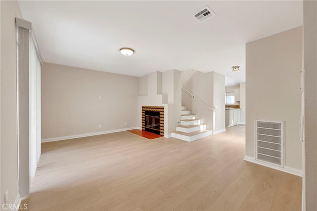 unfurnished living room with light wood-type flooring and a brick fireplace