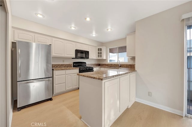 kitchen featuring kitchen peninsula, dark stone counters, black appliances, light hardwood / wood-style flooring, and white cabinetry