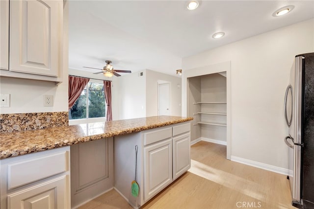 kitchen featuring white cabinets, ceiling fan, stainless steel fridge, and light stone counters